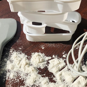 Pu&ograve; includere: Un set di tre tagliabiscotti in plastica bianca impilati uno sopra l'altro su una superficie di legno marrone. I tagliabiscotti hanno la forma di un rettangolo, un cerchio e una forma ondulata. C'&egrave; della farina bianca sparsa intorno ai tagliabiscotti.