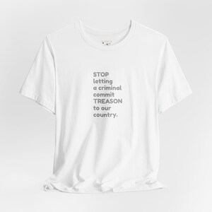 May include: White t-shirt with the text "STOP letting a criminal commit TREASON to our country" in gray. The shirt has a crew neck and short sleeves. The fabric appears to be cotton.