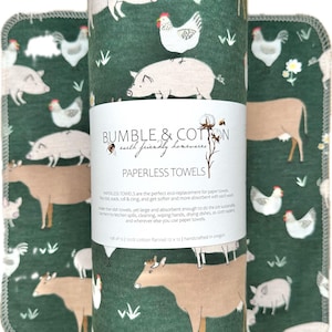 May include: Paperless towels with a farm animal print. The towels are rolled up and stacked, with a dark green background and images of pigs, cows, and chickens. The text "BUMBLE & COTTON earth friendly homewares" is visible.