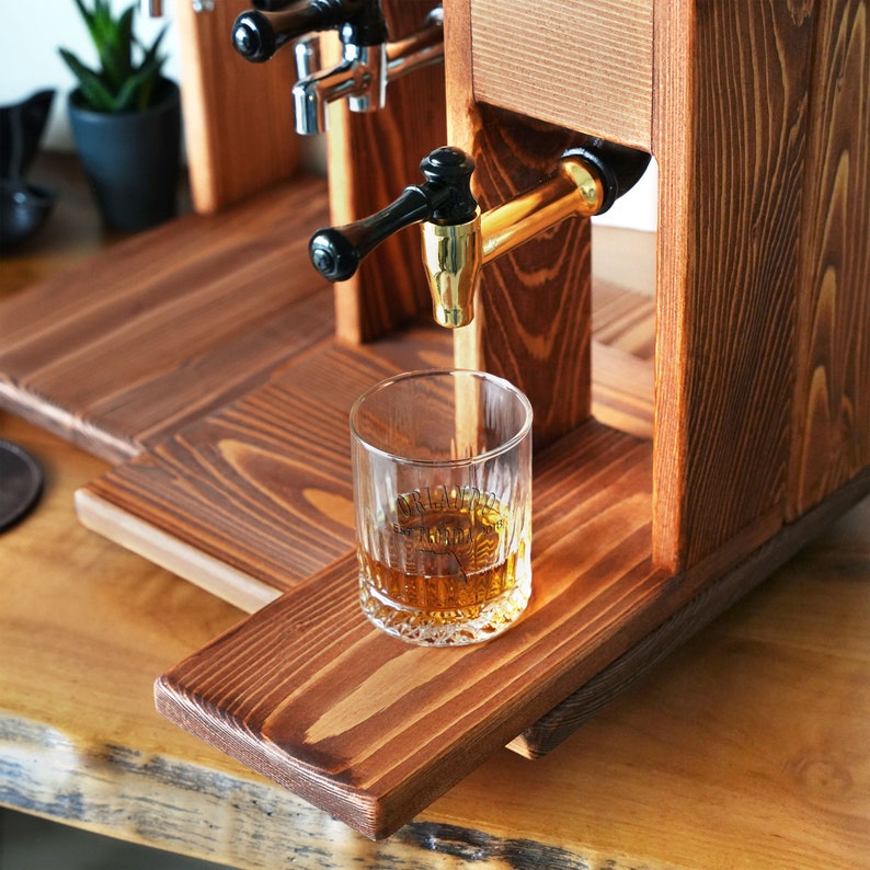 a glass of whiskey being poured into a wooden dispenser