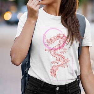 May include: White t-shirt with a pink and red dragon graphic. The dragon is curled around a pink circle.