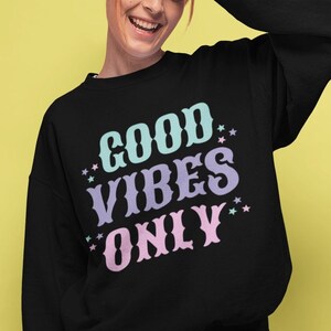 May include: Black sweatshirt with the text "GOOD VIBES ONLY" in pastel blue, purple, and pink lettering with white stars.