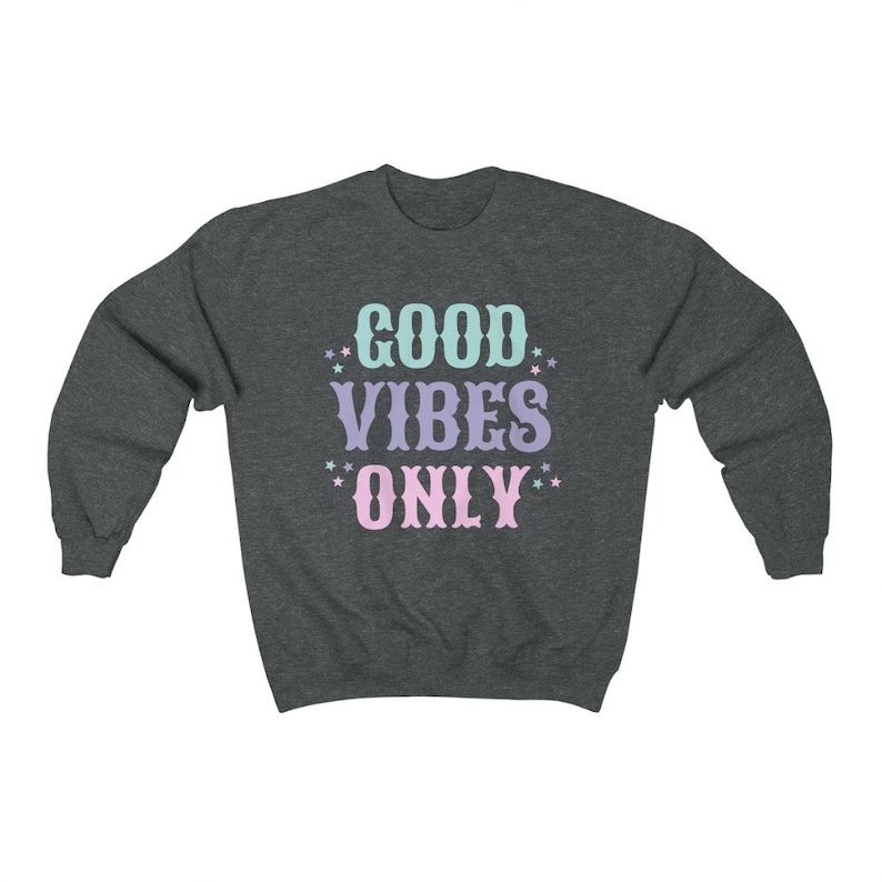 May include: A dark heather grey sweatshirt with the text "GOOD VIBES ONLY" in pastel pink, blue, and purple lettering with white stars around the text.