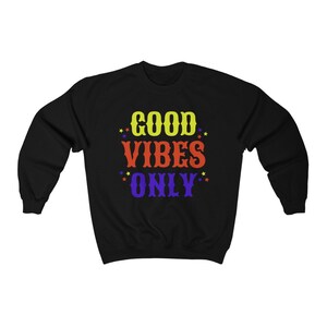 Op de afbeelding: Zwart sweatshirt met de tekst "GOOD VIBES ONLY" in gele, rode en paarse letters met kleine sterren rond de tekst.