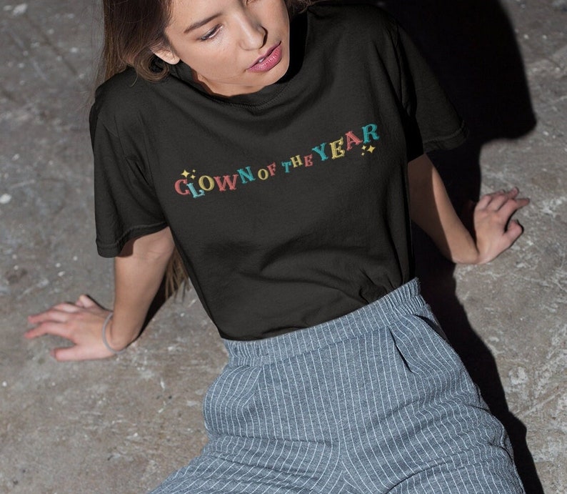 May include: A black t-shirt with the text "CLOWN OF THE YEAR" in colorful letters with stars on either side.