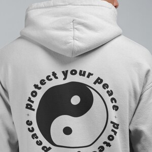 May include: A white hoodie with a black yin yang symbol and the text "Protect your peace + protect your peace" in a circle around it.