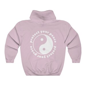 May include: A pink hooded sweatshirt with a white yin yang symbol and the text "Protect your peace - protect your peace" in a circle around it.