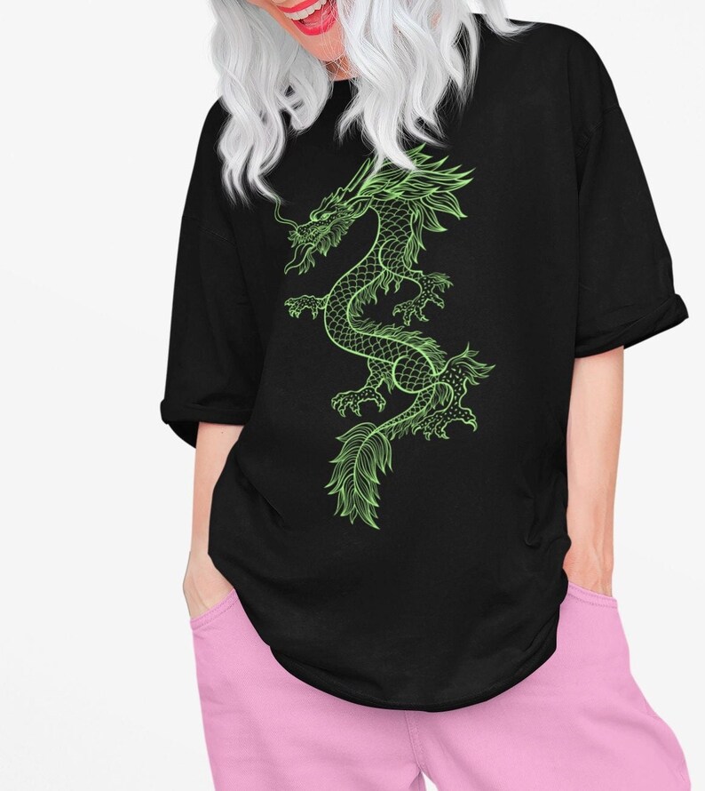 K&ouml;nnte beinhalten: Schwarzes, &uuml;bergro&szlig;es T-Shirt mit einem neongr&uuml;nen Drachendesign. Der Drache ist detailliert mit Schuppen und flie&szlig;enden Linien. Das T-Shirt ist l&auml;ssig geschnitten und f&uuml;r den Alltag geeignet.