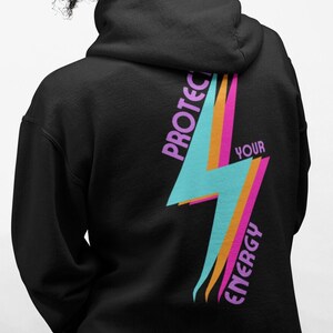 K&ouml;nnte beinhalten: Schwarzer Hoodie mit einem pinkfarbenen, orangen und blauen Blitz-Motiv auf der R&uuml;ckseite. Die Grafik sagt "Sch&uuml;tze deine Energie" in pinkfarbenem und wei&szlig;em Text.