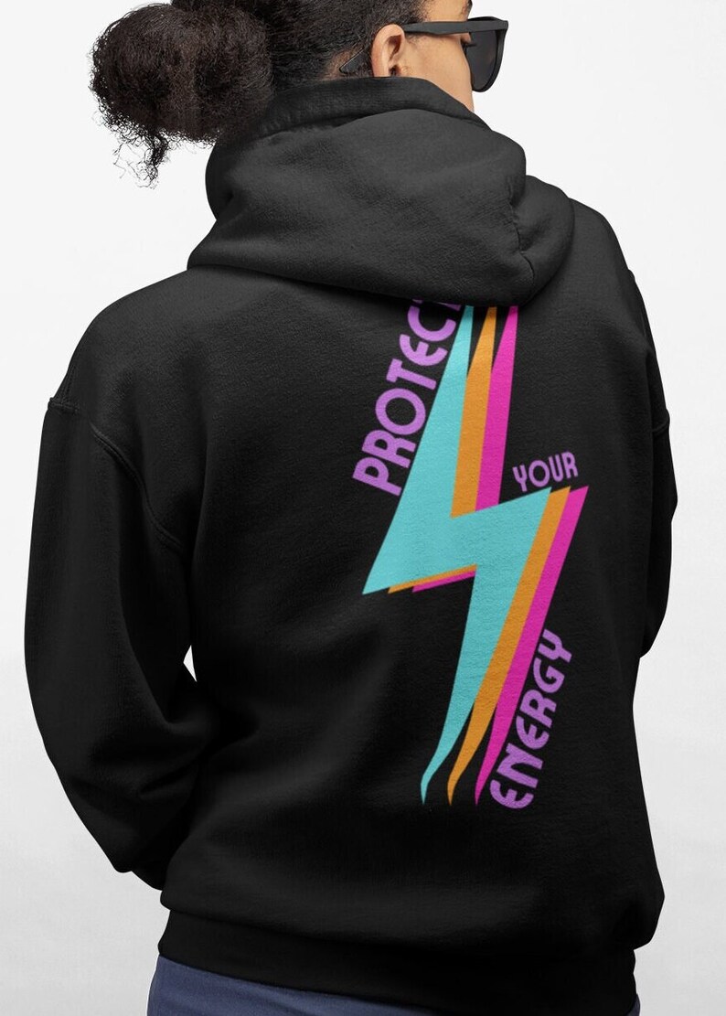 K&ouml;nnte beinhalten: Schwarzer Hoodie mit einem pinkfarbenen, orangen und blauen Blitz-Motiv auf der R&uuml;ckseite. Die Grafik sagt "Sch&uuml;tze deine Energie" in pinkfarbenem und wei&szlig;em Text.