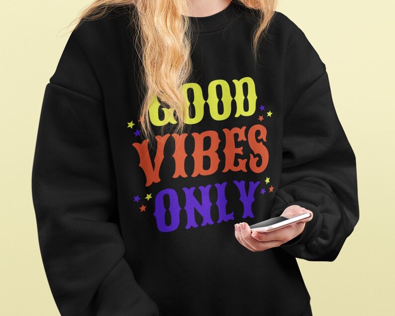 Op de afbeelding: Zwart sweatshirt met de tekst "GOOD VIBES ONLY" in gele, oranje en paarse letters met kleine gele sterren rond de tekst.
