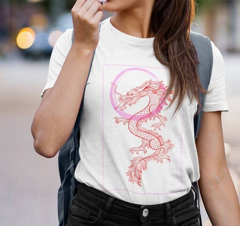 May include: White t-shirt with a pink and red dragon graphic. The dragon is curled around a pink circle.