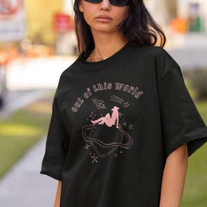 May include: Black t-shirt with a pink graphic of a woman sitting on a planet with the text "out of this world" above her.