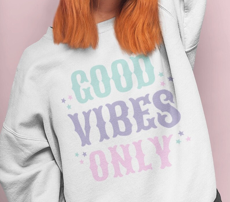 May include: White sweatshirt with the text "GOOD VIBES ONLY" in pastel colors with stars.