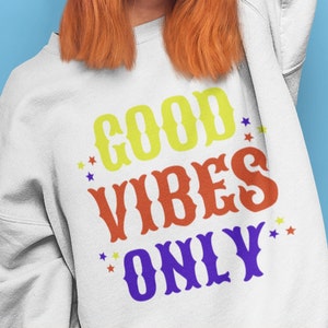 Op de afbeelding: Wit sweatshirt met de tekst "GOOD VIBES ONLY" in kleurrijke blokletters met sterren rond de tekst.