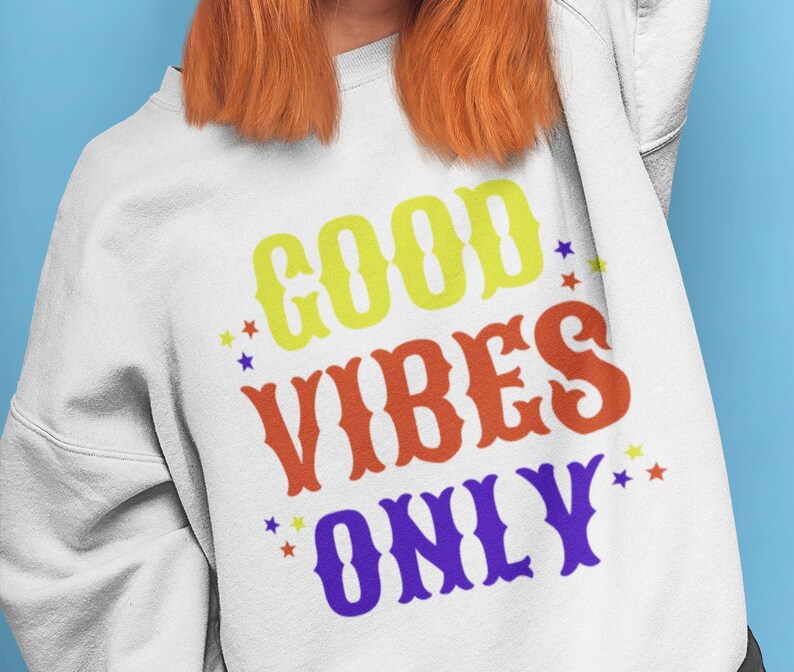 Op de afbeelding: Wit sweatshirt met de tekst "GOOD VIBES ONLY" in kleurrijke blokletters met sterren rond de tekst.