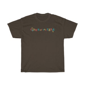 May include: A brown t-shirt with the text "CLOWN OF THE YEAR" in colorful letters with yellow stars on either side.