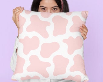Può includere: Un cuscino bianco con un motivo a stampa di mucca rosa. Il cuscino è tenuto da una persona, ma sono visibili solo i suoi occhi.