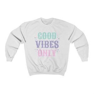May include: White sweatshirt with the text "GOOD VIBES ONLY" in pastel colors. The text is in a vintage style font with stars around it.