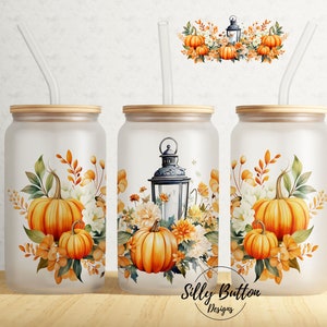May include: Three frosted glass tumblers with straw lids and straws. Each tumbler features a different fall-themed design with pumpkins, leaves, and flowers. The tumblers are on a wooden surface.
