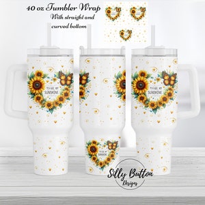 May include: A white 40 ounce tumbler with a handle and a straw. The tumbler has a design of sunflowers and butterflies in a heart shape with the text "You are my sunshine".
