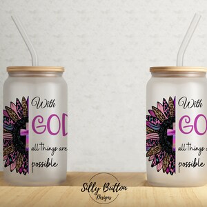 Puede incluir: Dos vasos de vidrio esmerilado con tapas y pajitas. Cada vaso presenta un girasol rosa y negro con una cruz en el centro. El texto "With God all things are possible" está impreso en cada vaso.
