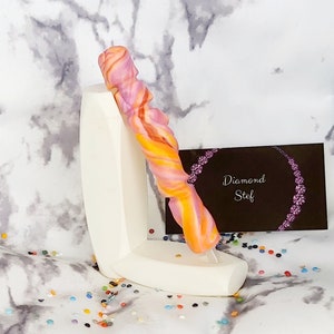 May include: A pink and orange swirl pen with a white pen holder. The pen holder has the text "Diamond Stef" on a black background.