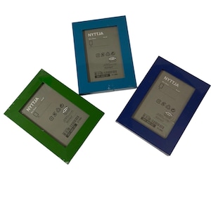 May include: Three rectangular picture frames in shades of green, blue, and navy. Each frame has a white interior and the text "NYTTJA" printed on the top left corner. The frames are 6" x 8" in size.