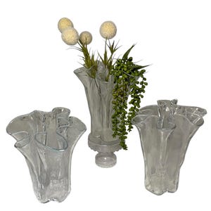 May include: Three clear glass vases with ruffled edges. The vases are arranged in a row, with the middle vase slightly taller than the others. The vases are empty, but they are ready to be filled with flowers.