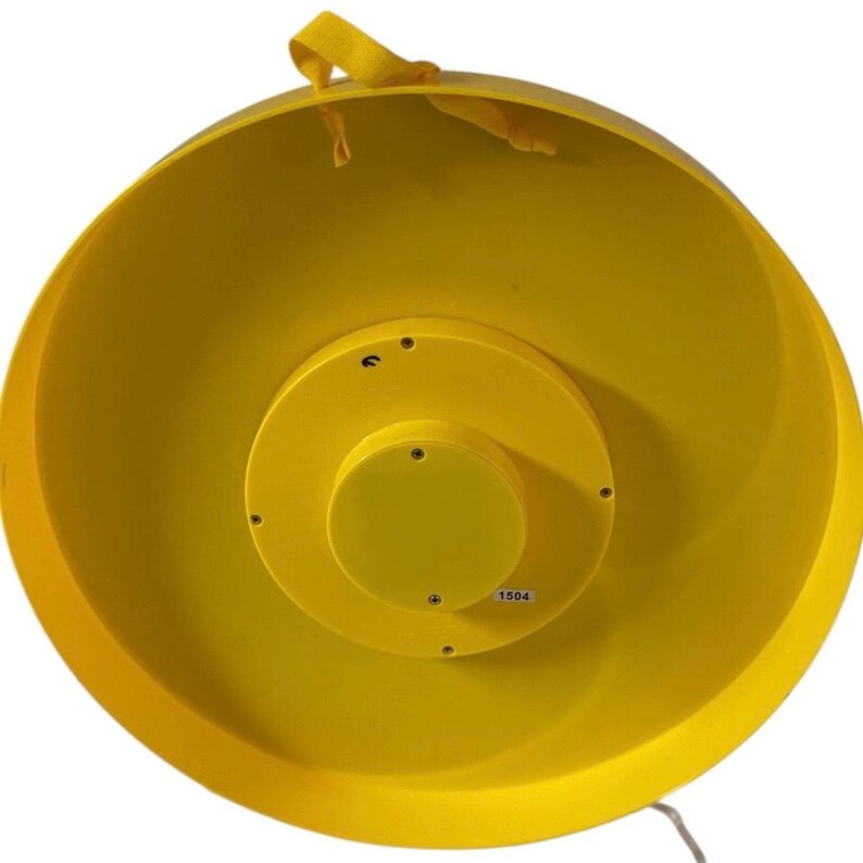 May include: A bright yellow, circular object with a central, raised, yellow disc. The object has a wide, shallow bowl shape with a loop of yellow fabric attached to the rim. The number "1504" is printed on the central disc.