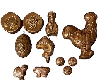 Op de afbeelding: Een verzameling van tien koperkleurige metalen vormen in diverse gedaantes, waaronder een grote haan, een vis, een kreeft, een ananas, fruit, een varken, een kleine vogel en drie kleine ronde vormen, elk voorzien van een metalen ophangoog.