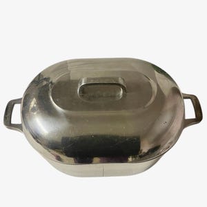 May include: A vintage Farberware stainless steel oval casserole dish with a lid. The dish has a handle on the lid and two side handles. The metal has a shiny, reflective surface.