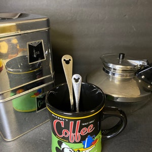 May include: Black coffee mug with a Mickey Mouse design. The mug features a green background with the text "Mickey's Coffee" and "Disney Blend".