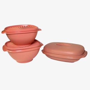 May include: A set of vintage peach-colored plastic food storage containers. The set includes two bowls with matching lids and a rectangular container with a lid. The lids have a textured design.