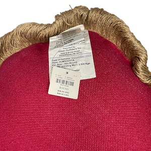 Puede incluir: Una almohada redonda de color rojo con un ribete de yute marr&oacute;n. La almohada tiene una etiqueta que dice "ROUND $58.00 USD $68.00 CAD".