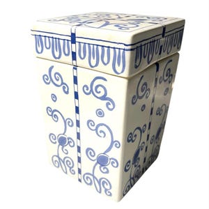 May include: A white ceramic box with a square shape and a matching lid. The box is decorated with blue scroll and dot patterns, and vertical blue stripes. The lid has a repeating blue design along the edge.