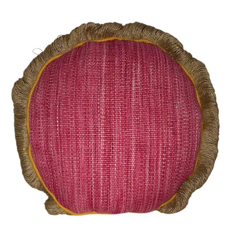 Puede incluir: Una almohada redonda de color rojo con un ribete de flecos dorados. La almohada est&aacute; hecha de una tela texturizada.