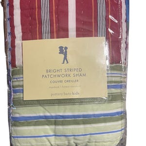 May include: A packaged patchwork sham with bright red, white, and orange stripes on the top half and green, blue, and white stripes on the bottom half. The label reads "BRIGHT STRIPED PATCHWORK SHAM COUVRE OREILLER standard / format standard pottery barn kids."