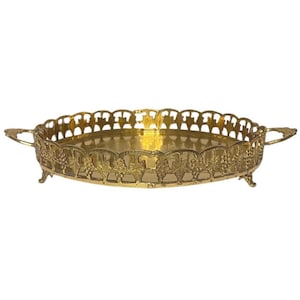 May include: A gold-colored, oval serving tray with ornate detailing. The tray features a scalloped edge and handles, with a decorative grape vine pattern around the sides. It rests on small feet.