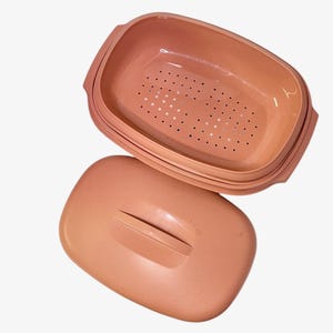 May include: A peach-colored rectangular colander with a matching lid. The colander has a perforated base and is designed for draining liquids. The lid features a handle for easy removal and placement. The kitchenware is made of plastic.