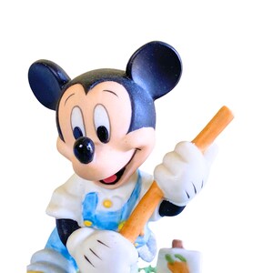 Peut inclure: Une figurine en c&eacute;ramique de Mickey Mouse portant une salopette bleue, tenant une carotte dans sa main droite. Il sourit et regarde vers la droite.