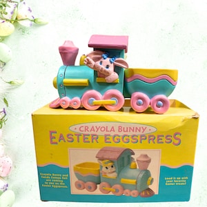 May include: A pink and blue toy train with a bunny on the front. The train is labeled "Crayola Bunny Easter Eggspress".
