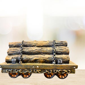 May include: A miniature wooden train car carrying a stack of logs, secured with chains. The car has four orange wheels and is painted in shades of brown and gold. The background is blurred with a bokeh effect.