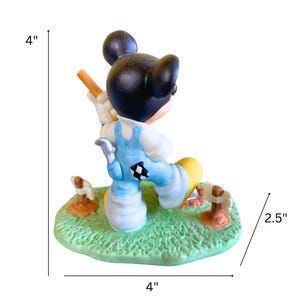Peut inclure: Une figurine en c&eacute;ramique de Mickey Mouse habill&eacute; d'une salopette bleue et d'un chapeau jaune, tenant une pelle et debout sur une base verte avec des accents bruns. La figurine mesure 10 cm de haut et 10 cm de large.