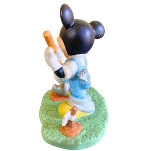 Peut inclure: Une figurine en c&eacute;ramique de Mickey Mouse habill&eacute; d'une salopette bleue et d'une chemise blanche, tenant un club de golf. Il est debout sur une base verte avec une balle de golf et un club de golf.
