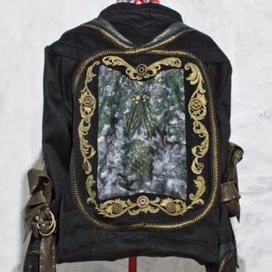 May include: A black denim jacket with a large gold embroidered frame featuring a green and white floral design.