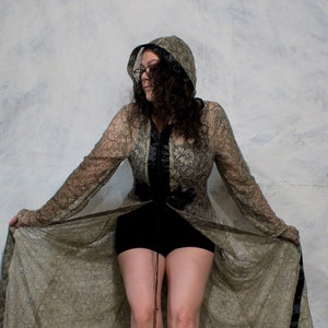 May include: A woman wearing a long, brown, lace dress with a black hood and black shorts. She is wearing teal and white patterned shoes.