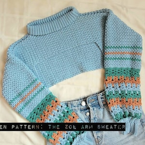 May include: A light blue crocheted sweater with a high neck and long sleeves. The sleeves feature a colorful striped pattern in shades of green, brown, and blue. The text "WRITTEN PATTERN: THE ZOE ARM SWEATER" is visible at the bottom of the image.