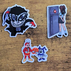 Puede incluir: Tres pegatinas con personajes de la serie Persona. La primera pegatina muestra una ilustración en blanco y negro del personaje Joker, con una máscara y sosteniendo un cuchillo. La segunda pegatina muestra una ilustración roja y blanca del personaje Jester, con un traje azul y blanco y sosteniendo una pierna de pollo. La tercera pegatina muestra una ilustración azul y blanca de una chica con uniforme escolar y de pie frente a una puerta.