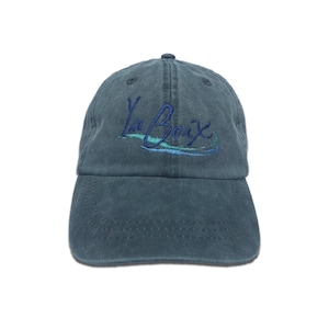 K&ouml;nnte beinhalten: Eine tealfarbene Baseballkappe mit dem gestickten Text "La Croix" in Schreibschrift. Die Kappe hat einen gebogenen Schirm und einen Stoffriemenverschluss. Die Kappe ist aus einem weichen, strapazierf&auml;higen Material gefertigt.